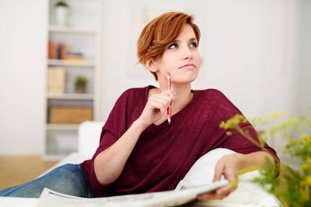 Thoughtful Attractive Young Woman Answering Crossword Puzzle Game on Newspaper at the Living Room Couch. Thoughtful Attractive Young Woman Answering Crossword Puzzle Game on Newspaper at the Living Room Couch.